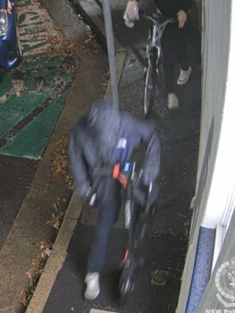 The second person is depicted as wearing a black ‘spray’ jacket with a white emblem in the left hand corner, black tracksuit pants, gloves which were possibly blue and orange in colour, white ‘Asics’ shoes. Picture: Supplied/ NSW Police.