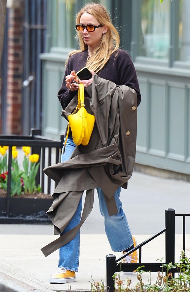 Jennifer Lawrence gave a low key outfit a pop of colour as she went for a walk in rainy New York. The actress wore a navy cardigan, blue jeans, daffodil-hued Vans and black rimmed sunglasses with yellow lenses while she carried a grey double-breasted trench coat over her arm. Picture: BACKGRID Australia