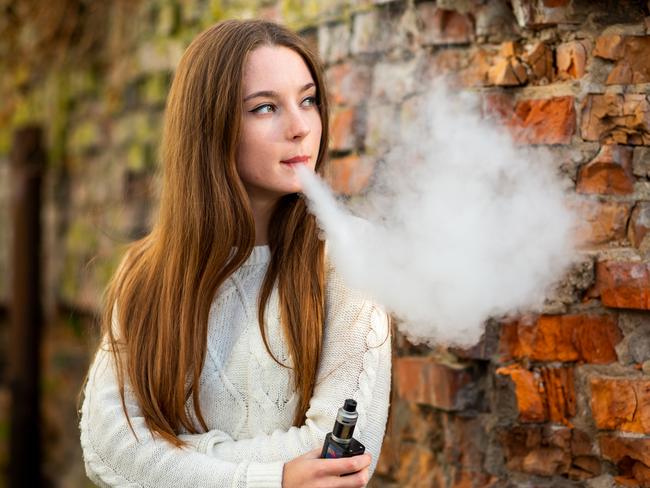 Vaping teenager. Young pretty white caucasian teenage girl with problem skin smoking an electronic cigarette the ruined brick wall on the street in the autumn. Bad habit. Vape activity.