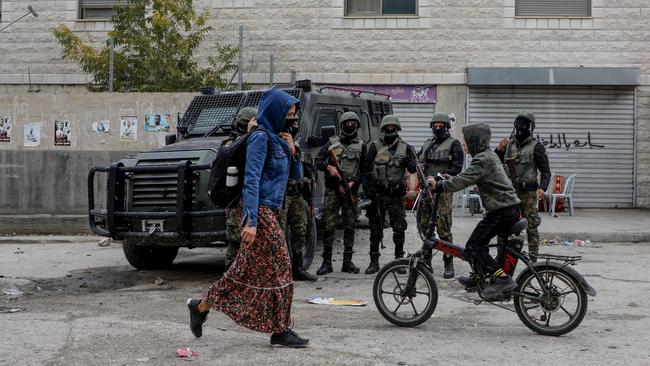 A Palestinian woman and a child riding a bicycle pass in front of members of the security forces in the Balata camp, near the occupied West Bank city of Nablus. Picture: AFP