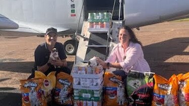 Royal Flying Doctor Service pilot Shaun Adamson holds one of the rescued puppies after he delivered a load of donated dog food to Burketown resident Paula McKinlay who is part of team who rescued abandoned canines after residents had to evacuate. Picture: Supplied