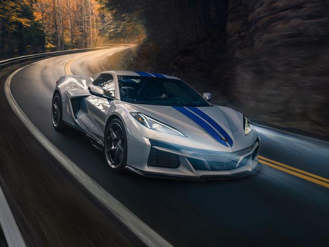 Passenger side front 3/4 view of 2024 Chevrolet Corvette E-Ray 3LZ convertible in Silver Flare with Electric Blue stripe package driving on a curved mountain road. Pre-production model shown. Actual production model may vary. Model year 2024 Corvette E-Ray available 2023.