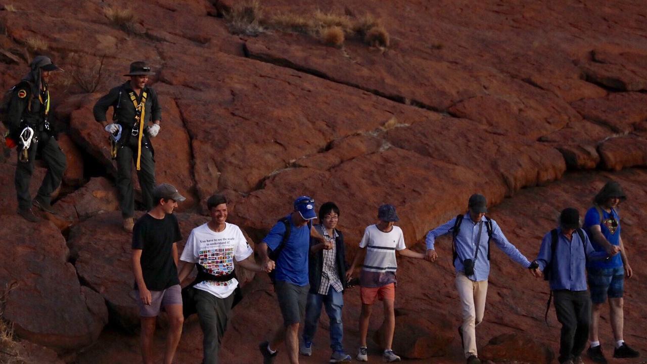 The last climbers — followed by two rangers — step off Uluru together.