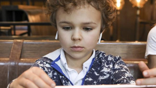 Six-year-old Grayson Hurd uses AirPods to watch shows on an iPad while his mother works at a New York restaurant. Picture: Bess Adler / The Wall Street Journal