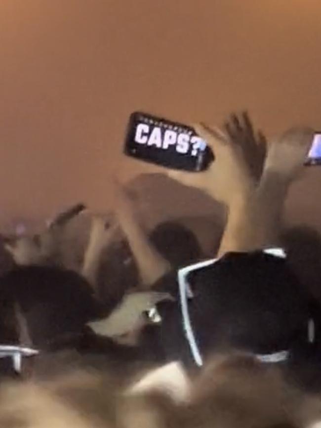 A reveller holding up his phone with the word ‘caps?’ on the screen.