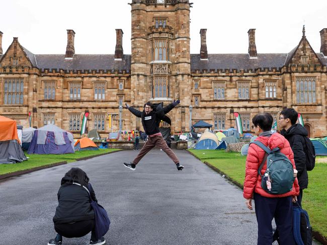 SYDNEY, AUSTRALIA - NewsWire Photos JUNE 15 2024. International students pose for pictures with the historic sandstone buildings of Sydney Uni, which are surrounded by a pro-gaza & Palestine tent camp. The uni has ordered the pro-Palestinian encampment to pack up and leave campus eight weeks after the tent protest appeared on its lawns. Picture: NewsWire / Max Mason-Hubers