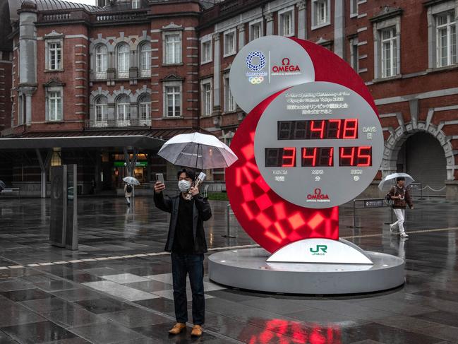 A man takes a selfie photograph next to a reset Tokyo Olympics countdown clock, which has been adjusted for the new start date of July 23rd, 2021.