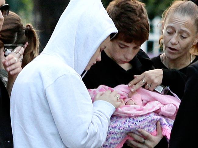 Jenifer Morrison, 15 (in White Hoodie) and her boyfriend, Jayden Lavender, 14 , holding baby Aria Jayde Tanya with his mother Tracy Lavender, carry the newborn towards a waiting ambulance after the young couple had  spent a night on the run with their newborn .The young couple were found at a property on Captain Cook drive in Willmott.