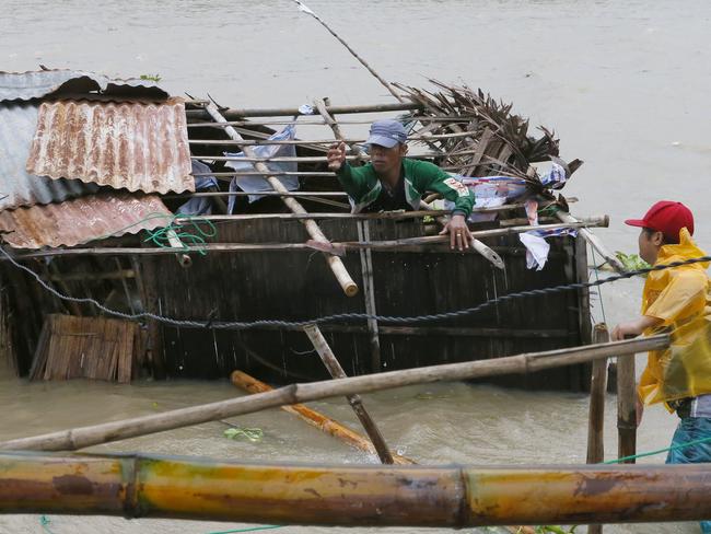 A fisherman fails to catch a nylon cable as he fixes his destroyed home amid flooding. Picture: AP
