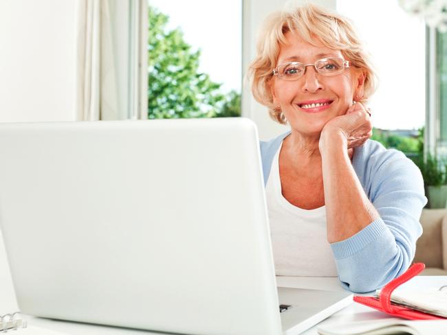 CAREERS FOR OCT 10: Mature woman sitting at the table at home with laptop in front of her and smiling at the camera.