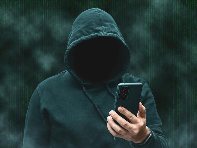 Mysterious faceless hooded anonymous hacker holding smartphone, silhouette of cybercriminal, terrorist.