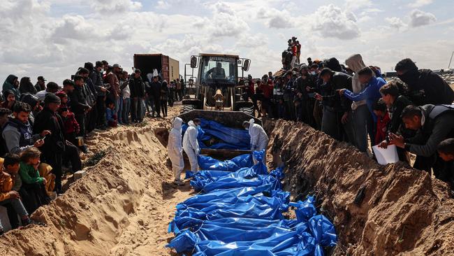 Mourners watch as medical personnel prepare the burial of bodies in Southern Gaza.