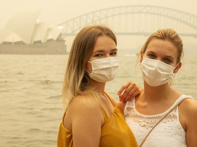 SYDNEY, AUSTRALIA - DECEMBER 19: German tourists Julia Wasmiller (L) and Jessica Pryor pose for a photo at Mrs Macquarie's chair, wearing face masks due to heavy smoke on December 19, 2019 in Sydney, Australia. NSW Premier Gladys Berejiklian has declared a state of emergency for the next seven days with ongoing dangerous fire conditions and almost 100 bushfires burning across the state. It's the second state of emergency declared in NSW since the start of the bushfire season. (Photo by Jenny Evans/Getty Images)