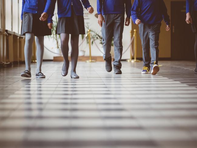 Cropped image of school kids in uniform walking together in a row through corridor. Focus on legs of students walking through school hallway.