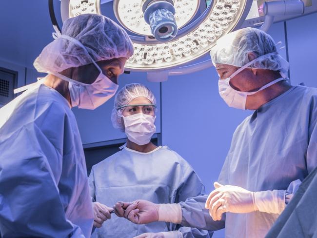 Doctors wearing surgical masks and gowns performing an operation on patient in hospital operating theater.