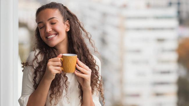 Happy business woman enjoying her hot beverage at work