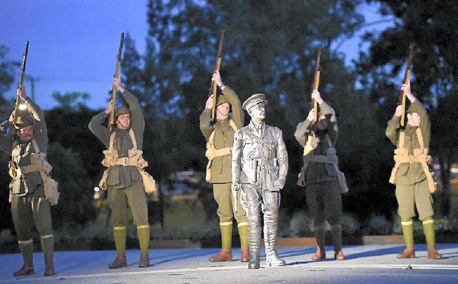 Members of the 9th Battalion AIF Living History Unit fire a salute behind the statue.