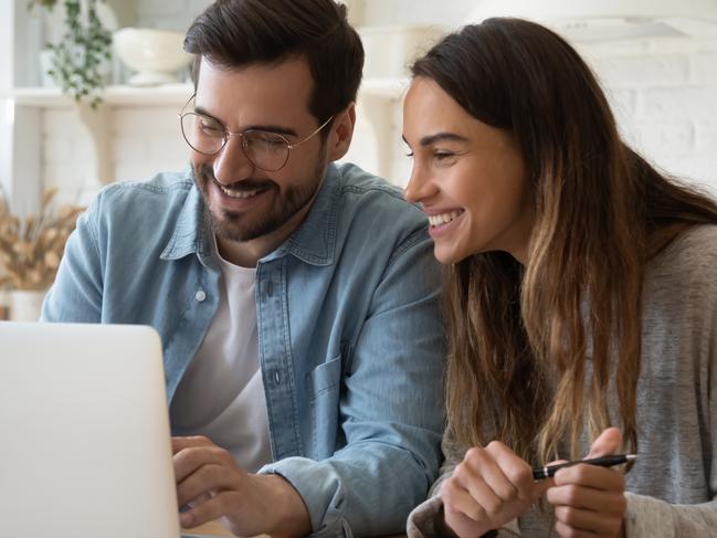 Happy young couple husband and wife using laptop computer looking at screen pay bills online including their home loan. Picture: iStock.