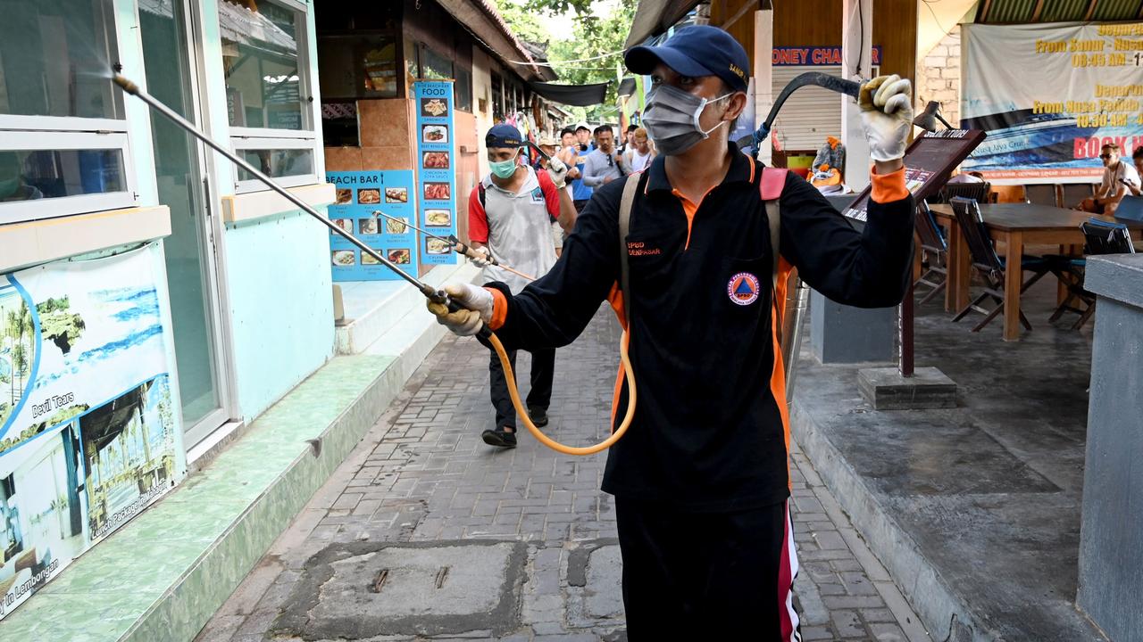 A healthcare worker in Bali sprays passers-by with disinfectant. Picture: Sonny Tumbelaka / AFP)