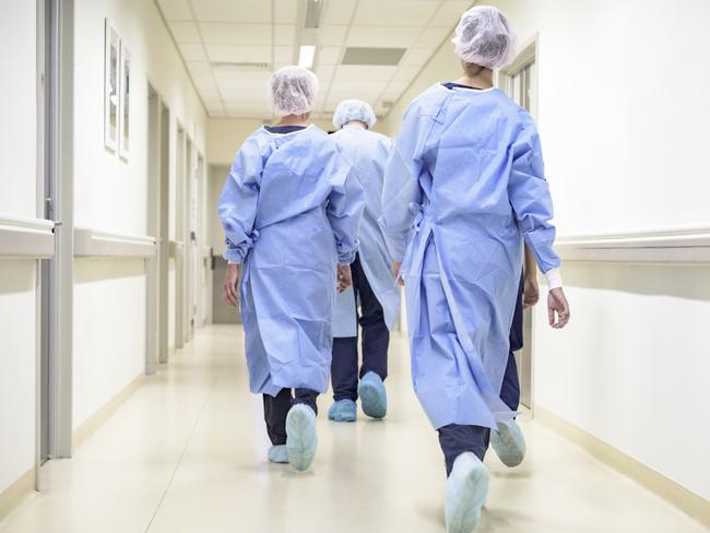 Rear view of male and female surgical team wearing gowns, caps, shoe covers, and walking down hospital corridor to operating room.