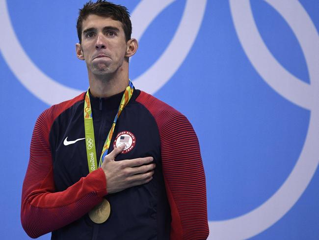 TOPSHOT - Gold medallist USA's Michael Phelps listens to his national anthem on the podium of the Men's 200m Individual Medley Final during the swimming event at the Rio 2016 Olympic Games at the Olympic Aquatics Stadium in Rio de Janeiro on August 11, 2016. / AFP PHOTO / Martin BUREAU