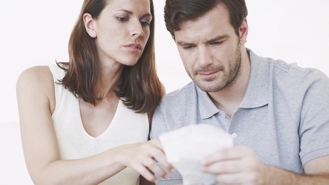 A married couple looking slightly concerned as they inspect bills and discuss their home finances