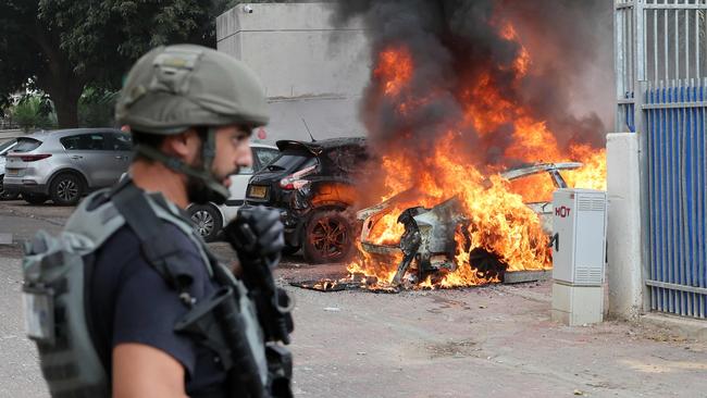 An member of the Israeli security forces stands close to a car hit by a rocket fired from Gaza, in the southern Israeli city of Sderot. Picture: AFP