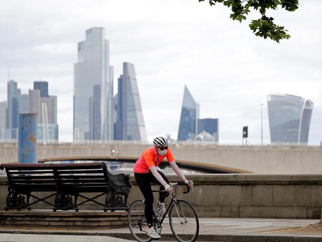 A man wearing PPE, cycles along Embankment, backdropped by the skyscrapers and office buildings of the City of London. Picture: AFP