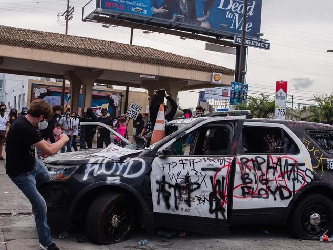 A demonstrator kicks a damaged police vehicle in Los Angeles. Picture: AFP