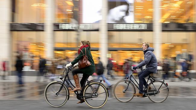 Two cyclists passing in front of the fashion shopping centre at dusk time. Bicycles are widely used in Antwerpen.