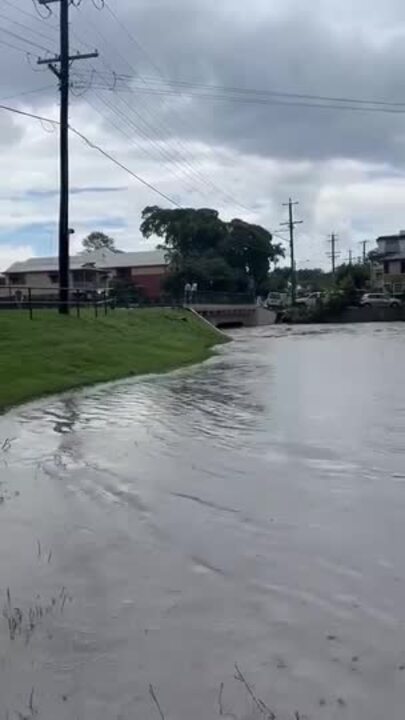 Flood water rushes through a park in Annerley