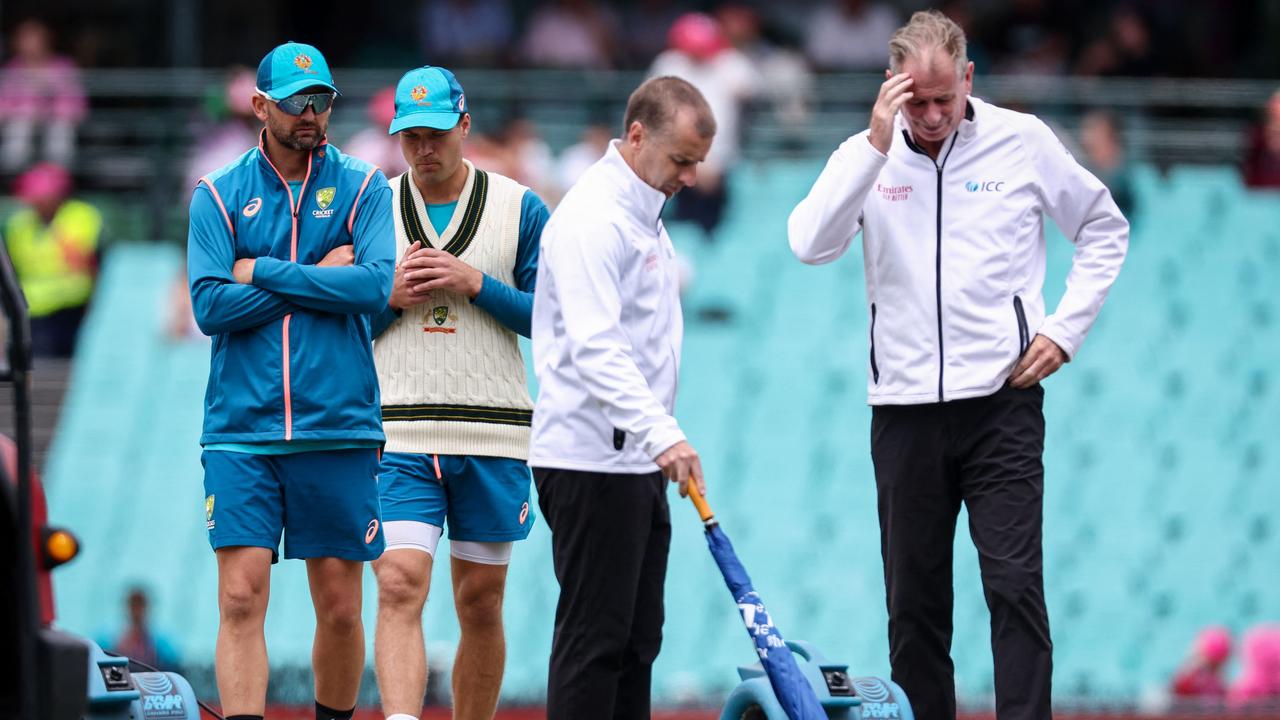 Australian players Nathan Lyon (L) and Alex Carey look on as umpires Paul Reiffel (R) and Chris Gaffaney inspect the pitch during a rain delay. Picture: AFP