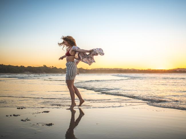 Young woman is spinning on the beach in the evening in Australia. She is having fun.