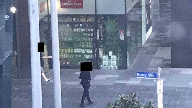 A quarantined guest walks out of the Pan Pacific in South Wharf, Melbourne, to go to a convenience store as a security guard, right, approaches.