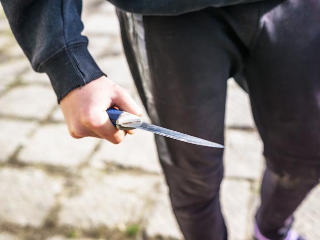 Close-up of a young man's hand with a knife, a big blade. Arrogance and violence among young people. Shallow depth of focus.