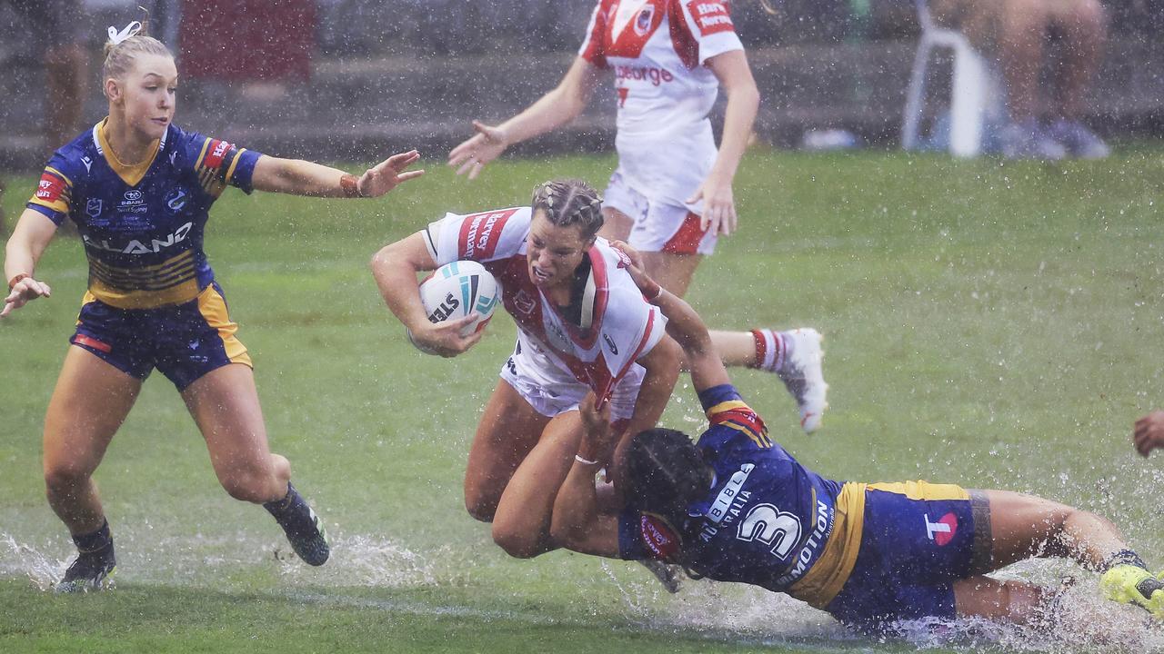 Olympic rugby gold medallist Emma Tonegato of the Dragons is tackled by Tiana Penitani of the Eels in the slippery conditions.