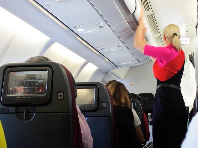 Brisbane - Oct 31 2022: Qantas airways female flight attendant closing the overhead luggage compartment lid for carry on baggage before take off.In Australia 1 flight attendant for every 36 passengers