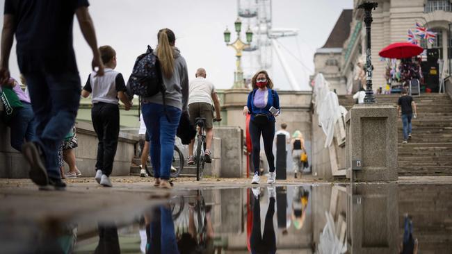 A woman wearing a face mask walks past a puddle on the Thames Embankment in central London. Picture: AFP