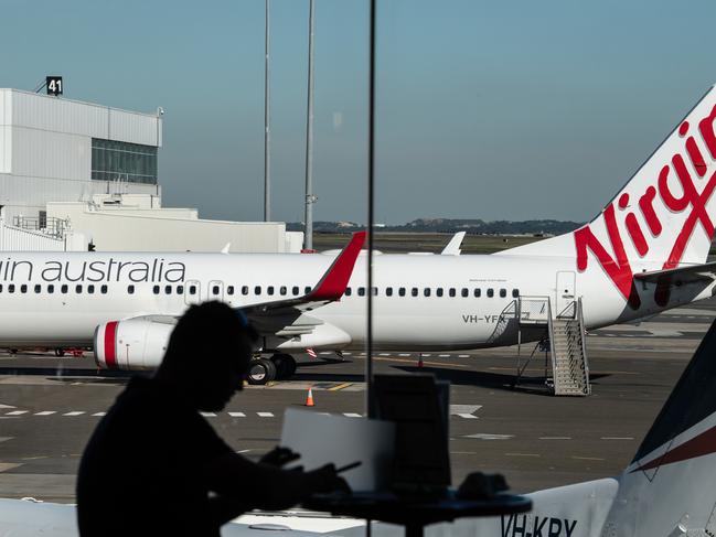 A man sits at a cafe in front of a Virgin Australia aircraft at Sydney Airport, Sydney, Friday, June 19, 2020. (AAP Image/James Gourley) NO ARCHIVING