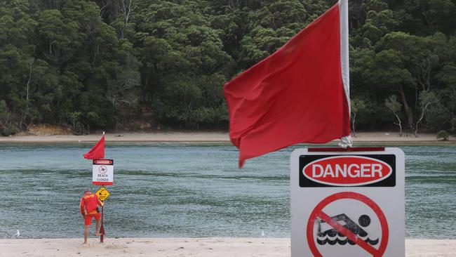 A lifeguard puts up warning signs on Tallebudgera Creek beach after stormwater outflows pollute the pristine waters with debris, causing a hazard to swimmers. Picture Glenn Hampson