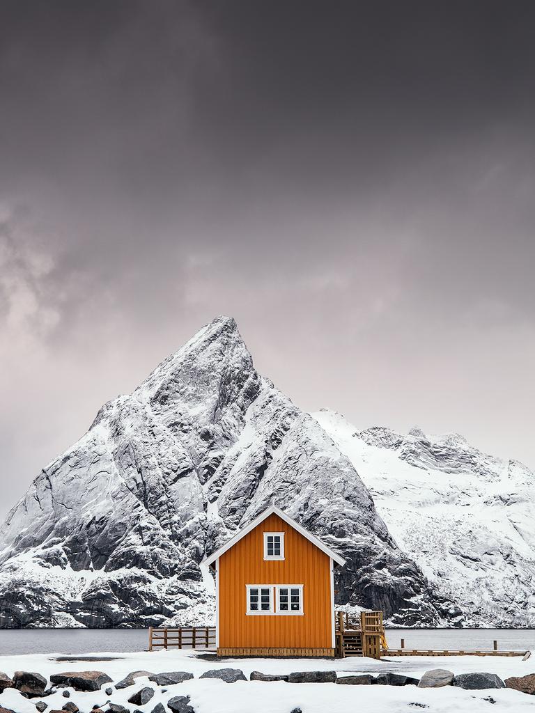 Image Name: Shapes of Lofoten Photographer Name: Mikkel Beiter Year: 2018 Image Description: I vintermånederne kan du se de mest fantastiske farvekontraster i Lofoten. De små klassiske hytter med deres gule og røde farver står i skarp kontrast til de hvide farver fra sneen samt den mørke vinterhimmel. Denne vinkel er helt speciel da den får hyttens tag til at følge formen på det ikoniske bjerg Olstinden som ses i baggrunden. Foto taget den 11. marts 2017, Sakrisøy i Lofoten, Norge. Copyright: Mikkel Beiter, Denmark, Winner, Open Travel and Denmark National Award. Picture: Sony World Photography Awards/ Mikkel Beiter