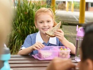 Cheerful school pupil sitting outdoors with packed lunch and eating healthy food