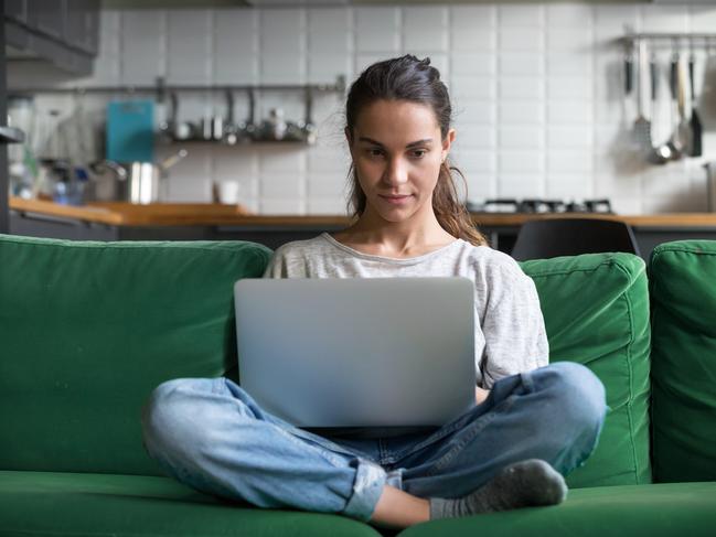 Serious woman using laptop checking email news online sitting on sofa, searching for friends in internet social networks or working on computer, writing blog or watching webinar, studying at home