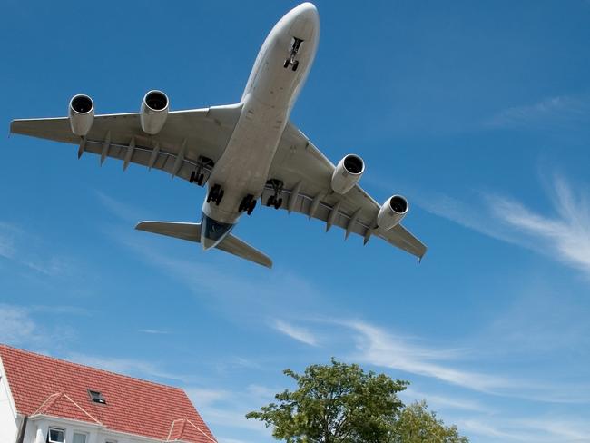 Large jet aircraft on landing approach over suburban housing.