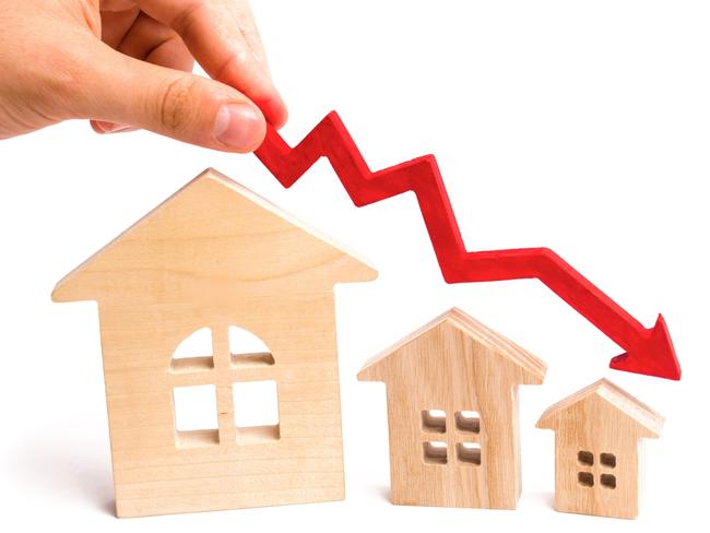 The hand holds a red arrow above the wooden houses down. The houses are decreasing. The concept of falling demand and supply in the real estate market. Economic crisis. The fall in prices.  iSTOCK image