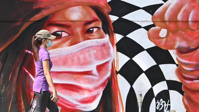 A mask-wearing woman walks past a mural depicting frontline health workers wearing masks, along a street in Manila on November 10, 2021. Photo by Ted ALJIBE / AFP.