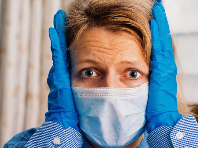 CORONAVIRUS: Picture: istock Worried person with virus protection surgical face mask and gloves holding her head in panic staying at home by the window