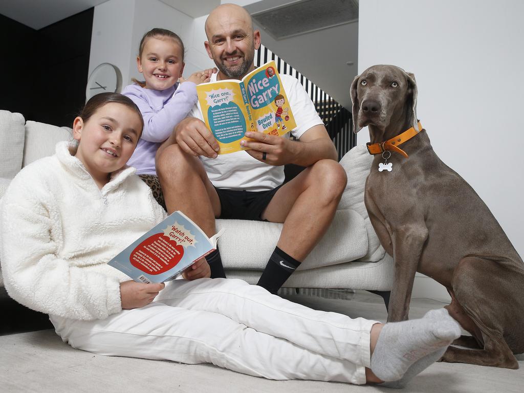 Nice one, Dad … Nathan Lyon shows his new books to daughters Harper, nine, and seven-year-old Milla, plus their dog Gus. Picture: John Appleyard