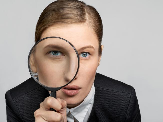 Portrait of a girl in the office at work looks carefully into the magnifying glass with one eye. The concept of office work and search. tax generic