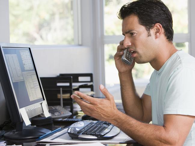 Man in home office on telephone using computer and frowning. For letters page. Computer problem generic